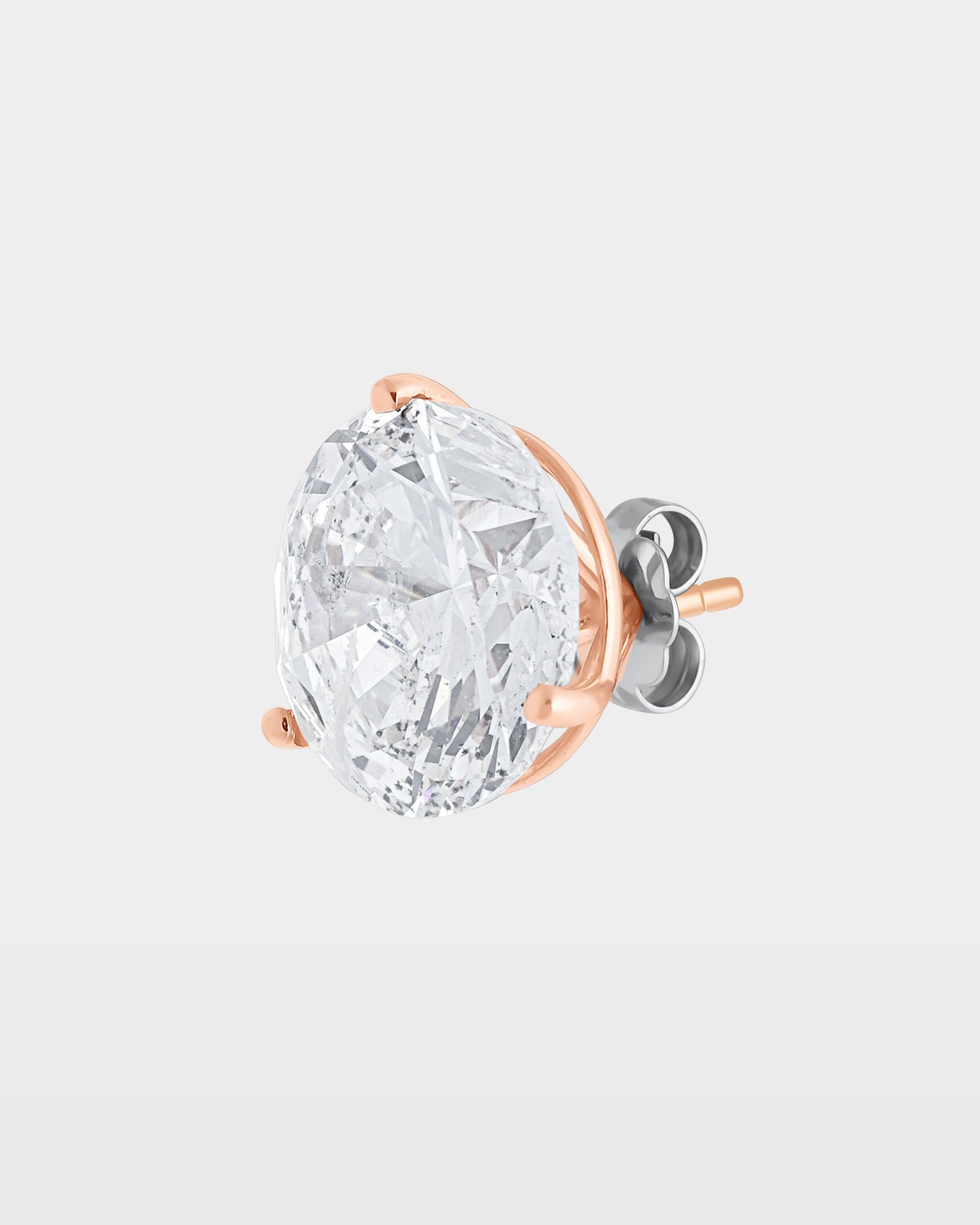 An angled studio macro shot of a single massive round brilliant diamond solitaire stud earring in a 14k rose gold 3-prong basket setting
