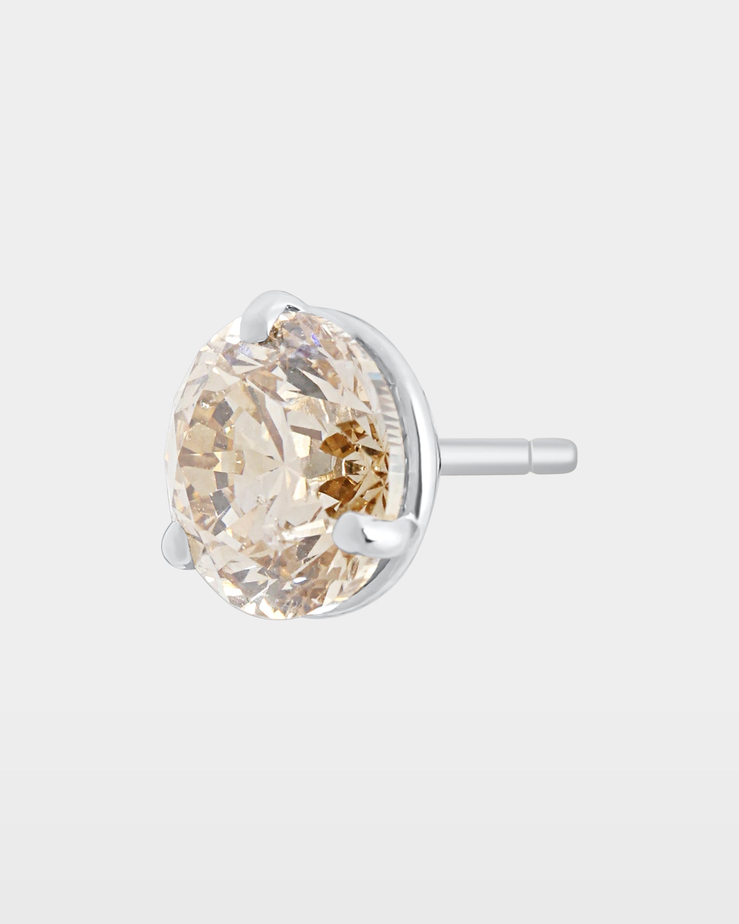 angled studio macro shot of a single round champagne diamond solitaire stud earring with the 3 prong martini basket profile