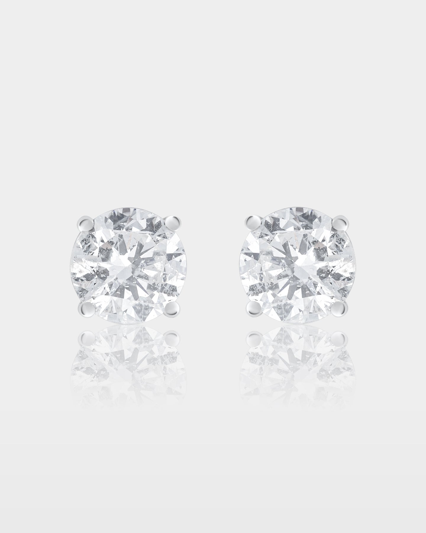 A pair of classic round brilliant-cut diamond solitaire stud earrings set in a traditional 14k white gold four-prong basket setting