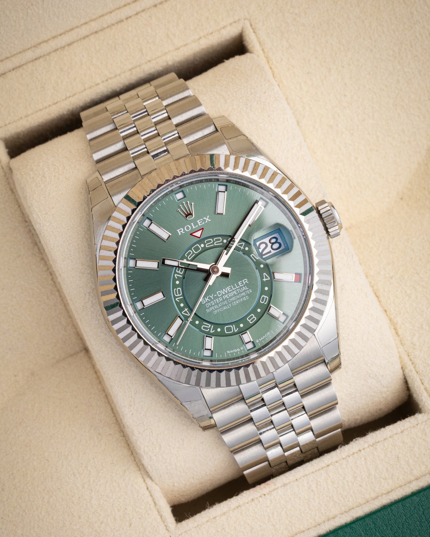 angled studio view of a white Rolesor Rolex Sky-Dweller with a mint green dial resting on a cream watch presentation pillow